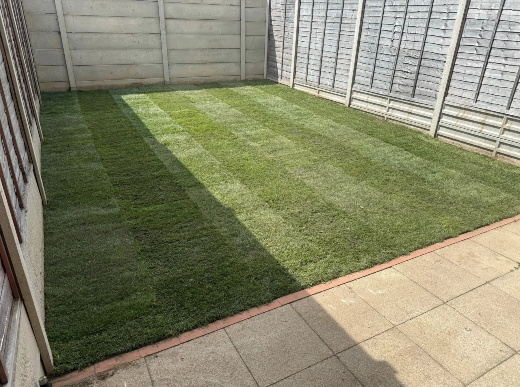 New lawn with paving border and tidy garden fence