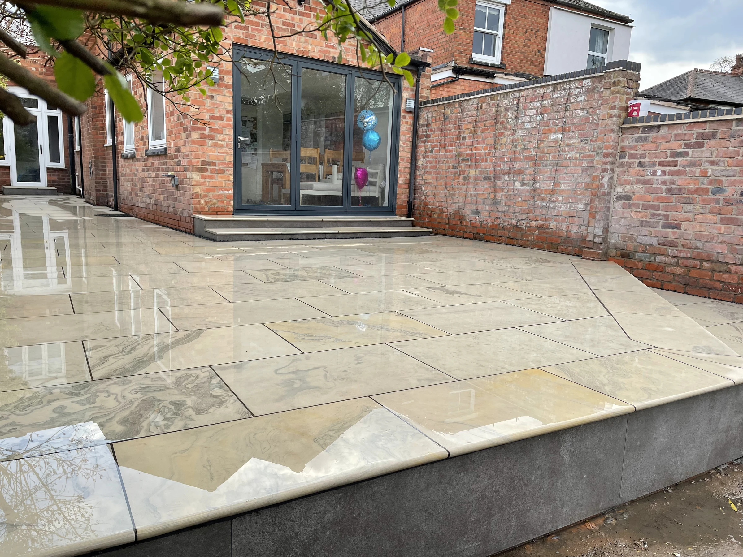 Premium stone patio with a raised edge beside a brick home