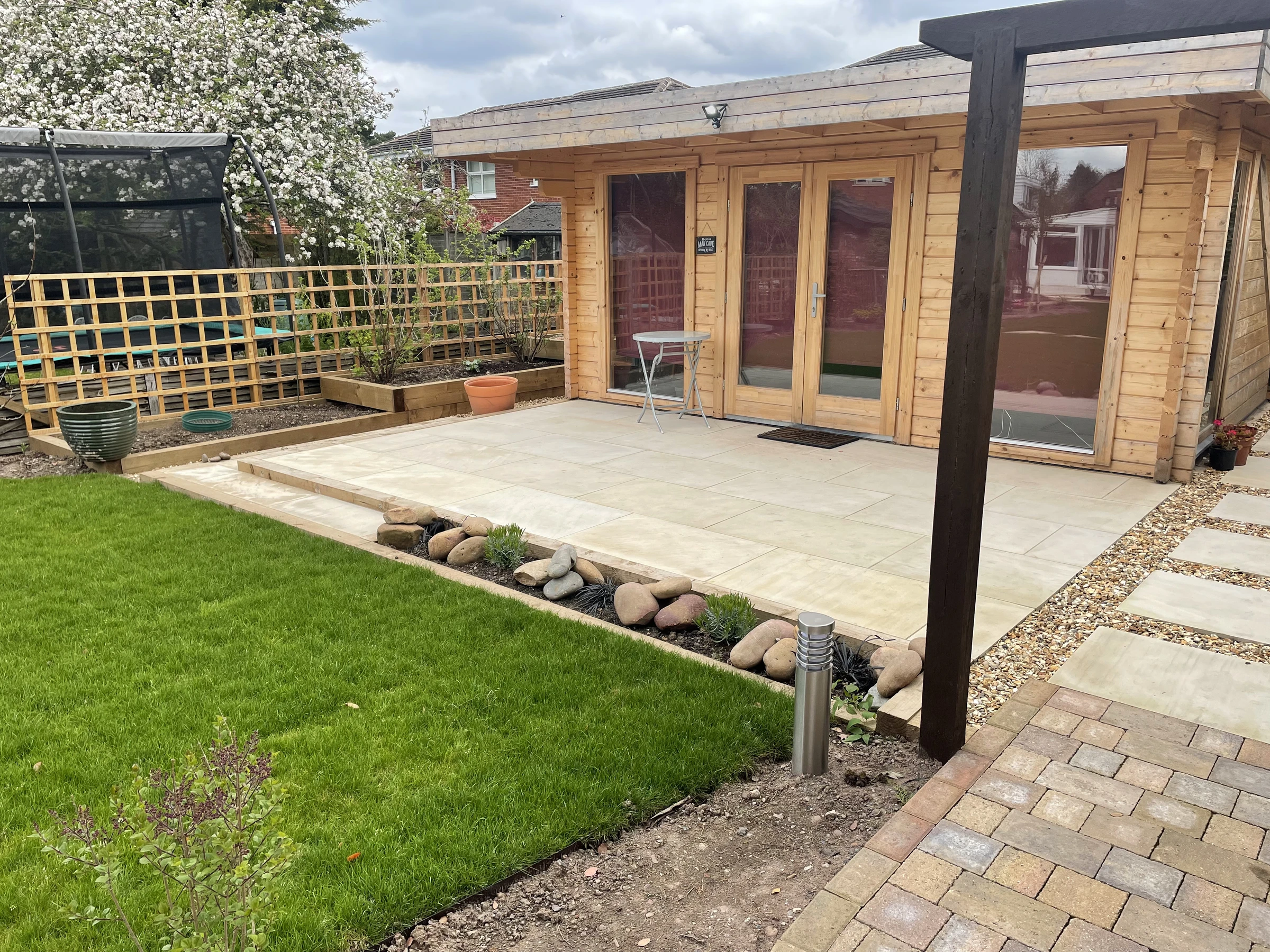 Completed stone patio beside a timber garden building and fresh lawn