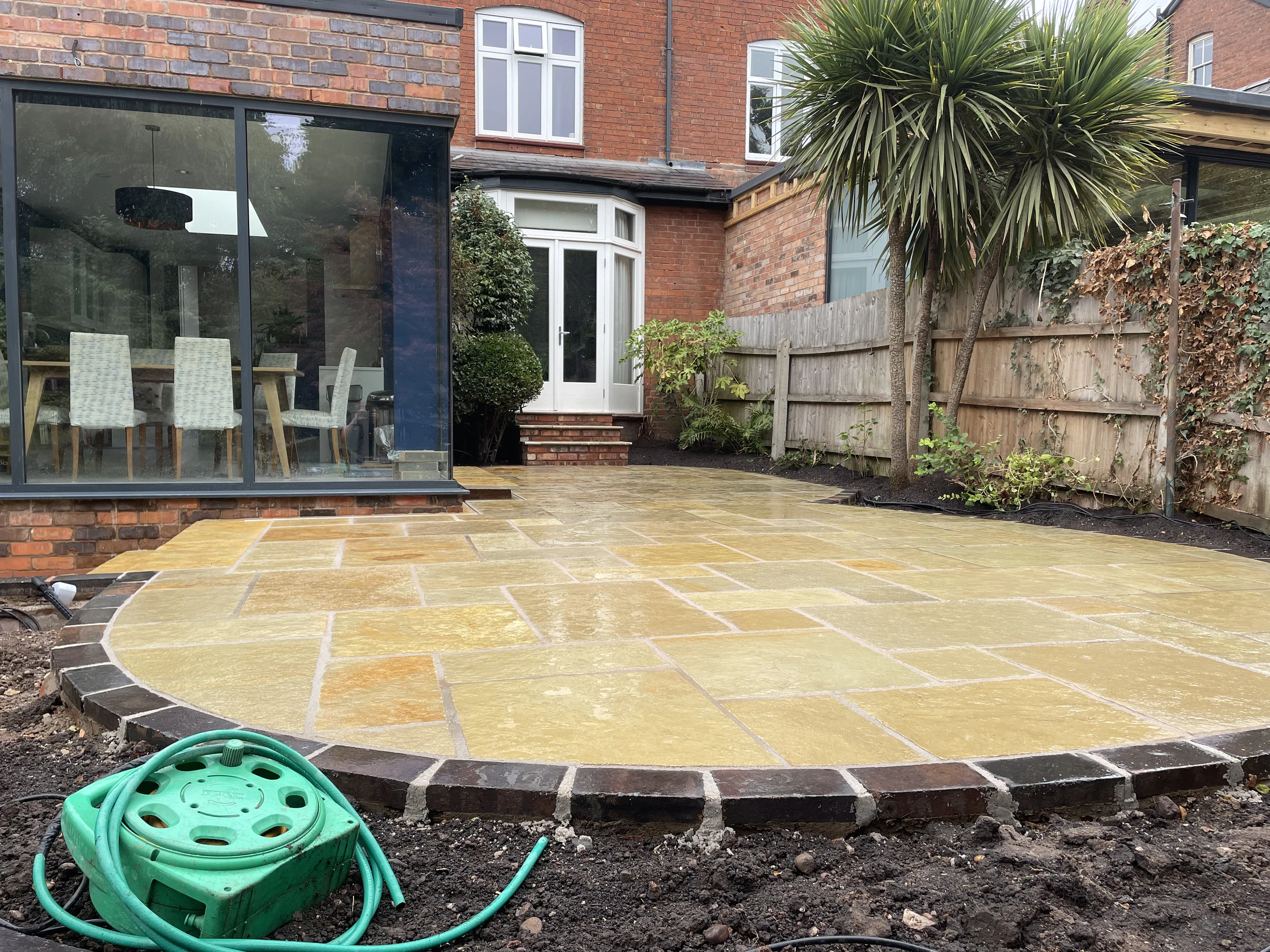 Curved stone patio with brick edging beside a home and planted borders