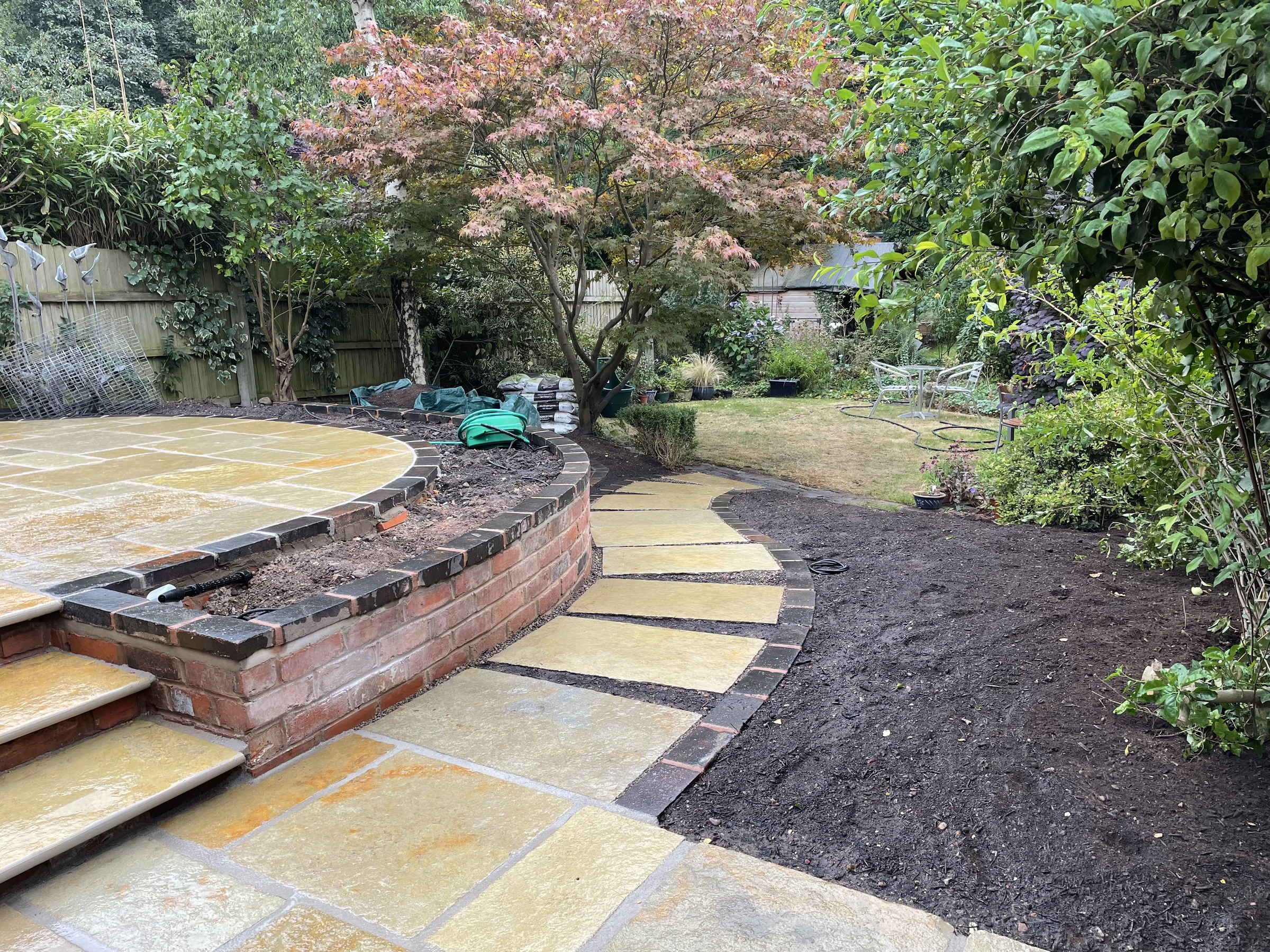Curving stone pathway beside a raised patio, brick wall and garden planting